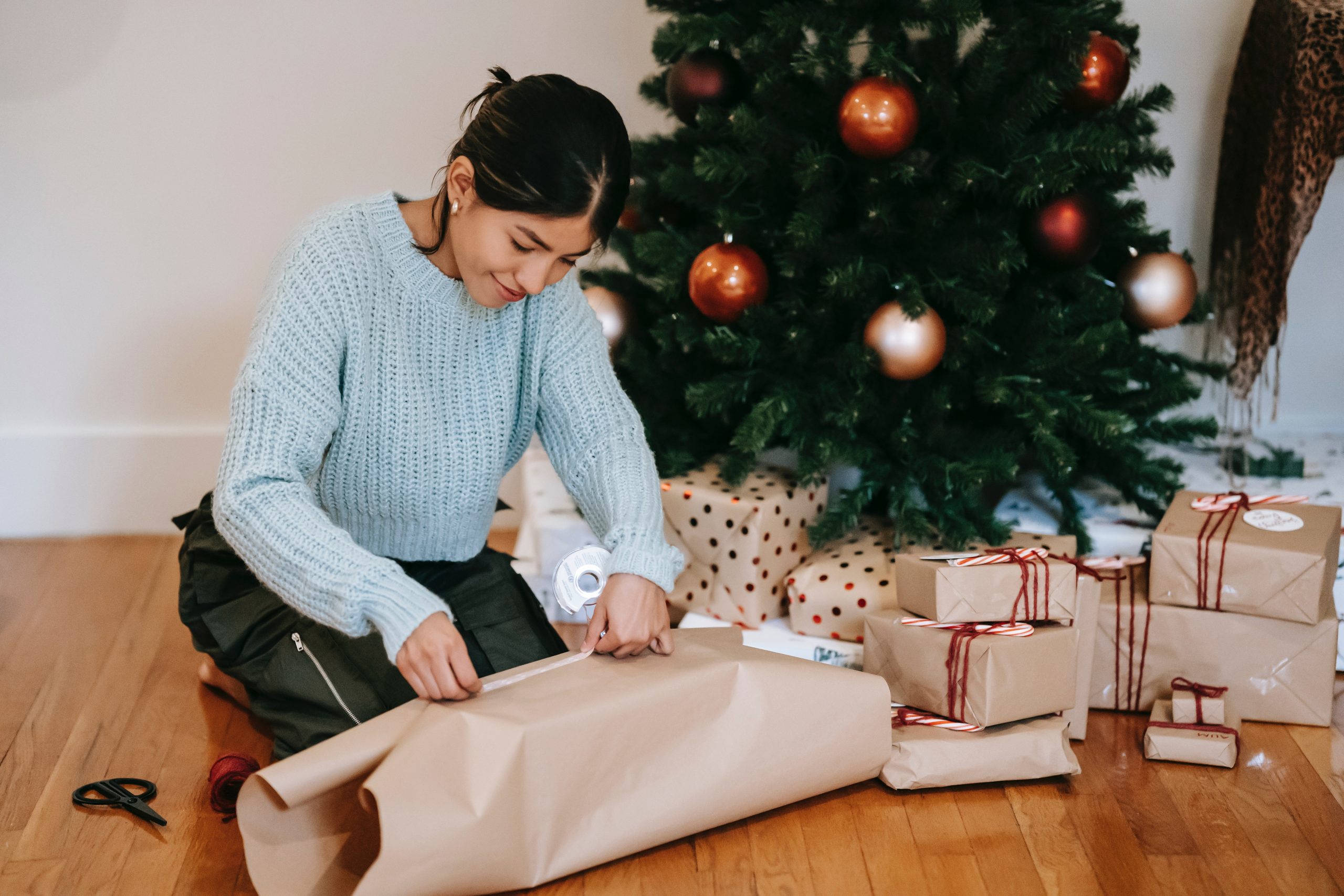 woman wrapping present box near christmas tree
